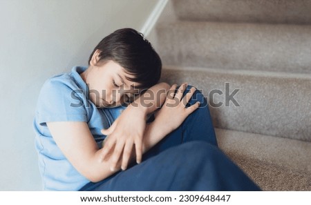 Sad School kid sitting alone on staircase in the morning, Lonely boy looking dow with sad face not happy to go back to school, Depressed child boy sitting in the corner of a stair,Mental health