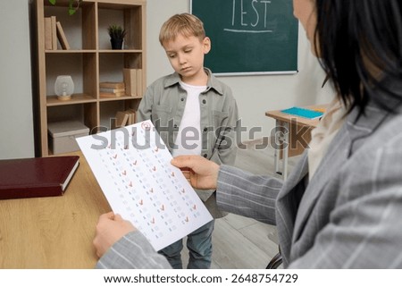 Sad schoolboy receiving answer sheet with D grade from teacher in classroom