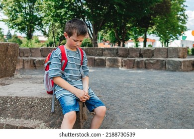 A Sad Schoolboy Sits In The School Yard With A Backpack On His Back. Children's Problems At School. The Boy Does Not Want To Go To School