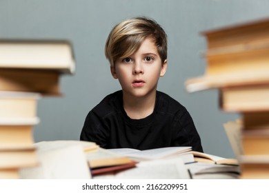 A sad schoolboy sits at a table with a pile of books. Cute boy in a black t-shirt. Difficulties in learning and stress. Gray background.  - Powered by Shutterstock