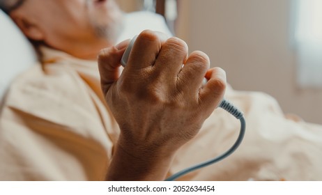 Sad senior Asia man having having heart attack lying on hospital bed and press emergency button. Sick aged guy lying hospitalized in a medical clinic. Health insurance or hospitality concept.