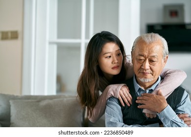 sad senior asian father sitting on couch in living room at home consoled by adult daughter - Powered by Shutterstock