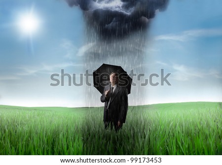 Sad senior businessman on a green meadow with downpour over him and sunny sky in the background