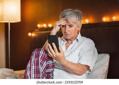 Sad Senior Lady Using Mobile Phone At Home, Sitting On Couch, Covering Face With Hand. Frustrated Upset Mature 60s Woman Holding Smartphone, Reading Message, Making Video Call, Getting Bad News