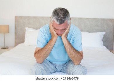 Sad Senior Man With Head In Hands Sitting On Bed At Home