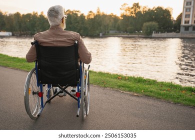 Sad senior man sitting in wheelchair walking on road in city park outdoor, back view. Old paralyzed man in chair for people with disability feel depressed. Lonely elderly sick man sits on wheelchair - Powered by Shutterstock