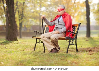 Sad Senior In Superhero Outfit Sitting In Park On A Wooden Bench