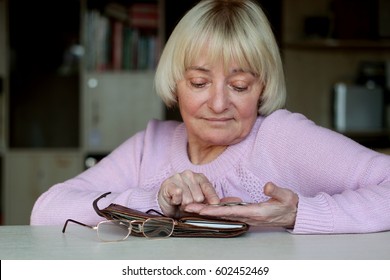 Sad Senior Woman, An Elderly Pensioner Counting Coins On Her Palm, Wallet With Money, Eye-glasses At The Table, Concept Of Financial Security In Old Age, Indoor Portrait, Focus On The Hand With Coins