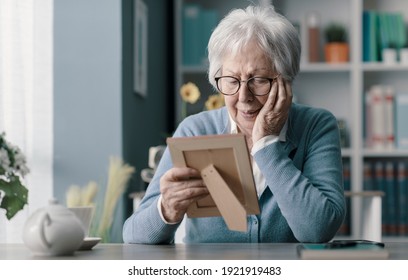 Sad senior woman mourning the loss of her husband, she is holding a picture and crying - Powered by Shutterstock