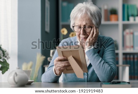 Sad senior woman mourning the loss of her husband, she is holding a picture and crying