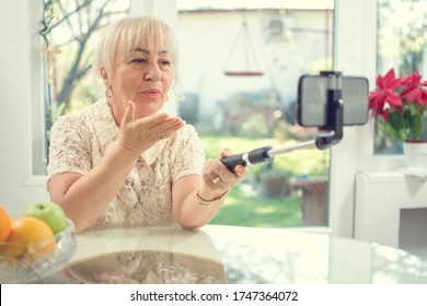 Sad Senior Woman Sending A Kiss To Her Family During Emotional Video Call, Holding Selfie Stick Monopod With Smartphone.