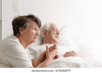 Sad senior woman sitting next to her dying husband in hospital