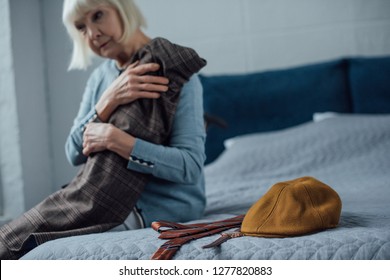 sad senior woman sitting on bed and holding jacket at home - Shutterstock ID 1277820883