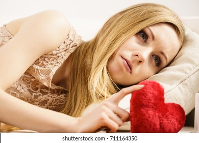 Sad Or Serious Woman Feeling Lonely And Unloved Holding Little Red Pillow In Heart Shape.