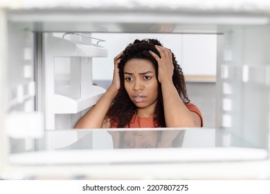 Sad Shocked Hungry Millennial Black Lady Hold Her Head, Looking Into Empty Refrigerator, Suffering From Starvation And Poverty In Kitchen, Close Up. Facial Expression, Stress Emotions, Food Problems