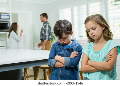 Sad siblings standing with arms crossed while parents arguing in background at home - Powered by Shutterstock