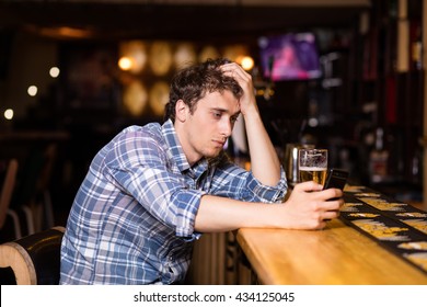 Sad Single Man Drinking Beer At Bar Or Pub, Using His Cellphone, Texting Or Betting