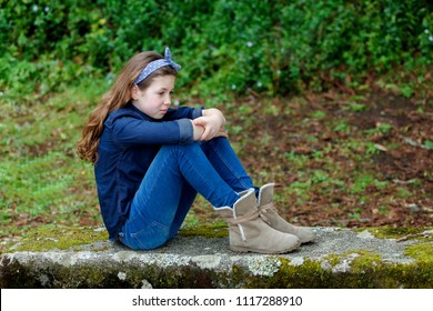Sad small girl with ten years old wearing a blue hair scarf sitting on a bench