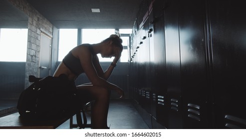 Sad sporty Caucasian woman sitting alone in dark gym locker room, feeling lost and upset overcoming failure slow motion. - Powered by Shutterstock