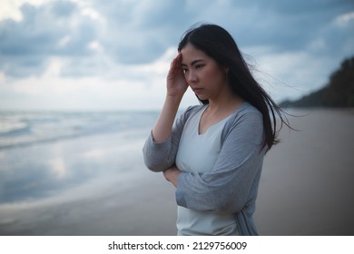 A sad and stressed Asian woman stands alone on the beach in the evening. Dramatic atmosphere. disappointment in life. She stood crying alone