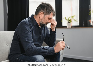 Sad stressed troubled mature middle-aged man sitting on the couch, missing his friends, feeling bad unwell unhealthy, suffering from depression at home. - Powered by Shutterstock