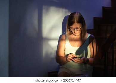 Sad Stressed Woman With Telephone. Depression And Anxiety. Senior Female Sitting On Stairs Step In Dark Room Feeling Depressed And Tired. Stress And Mental Health Concept.