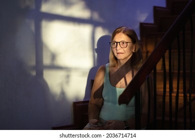 Sad Stressed Woman With Telephone. Depression And Anxiety. Senior Female Sitting On Stairs Step In Dark Room Feeling Depressed And Tired. Stress And Mental Health Concept.