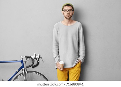 Sad student holding takeaway coffee, wanting to sleep after sleepless night, preparing for final exams, going to university with bad mood, standing near his transport. Hipster boy with coffee isolated