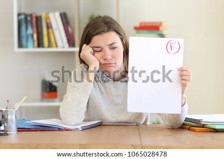 Sad student showing a failed exam to camera at home