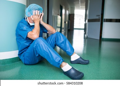 Sad Surgeon Sitting On Floor In Corridor At Hospital. Healthcare Workers In The Coronavirus Covid19 Pandemic
