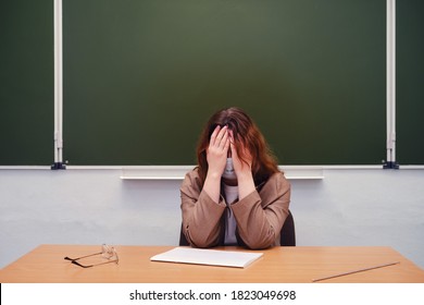 Sad teacher sits in a school classroom, copy space - Shutterstock ID 1823049698