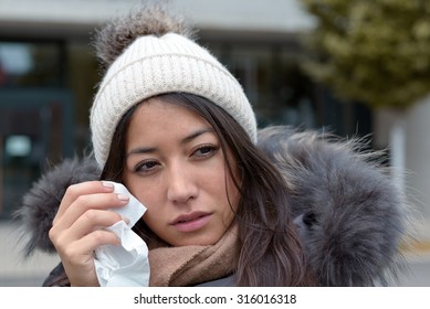 Sad Tearful Woman In Warm Winter Fashion Holding A Handkerchief To Her Face To Dry The Tears From Her Eyes Looking To The Right Of The Frame With Lack Lustre Eyes And Woebegone Expression