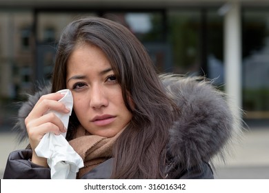 Sad Tearful Woman In Warm Winter Fashion Holding A Handkerchief To Her Face To Dry The Tears From Her Eyes Looking Into The Camera