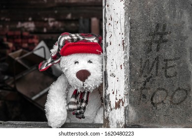 A Sad Teddy Bear In A Red Hat Is Looking Out Of The Window Of An Old House. The Inscription On The Window # Me Too. The Concept Of Violence, Abandonment, Sexual Abuse.
