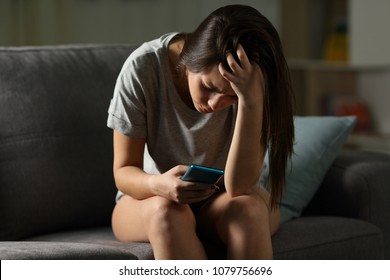 Sad Teen Being Victim Of Cyber Bullying Online Sitting On A Couch In The Living Room At Home