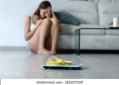 Sad Teen Complaining About Her Body Weight Sitting On The Floor With A Scale In Foreground