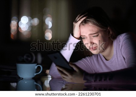 Sad teen crying checking phone in the night at home