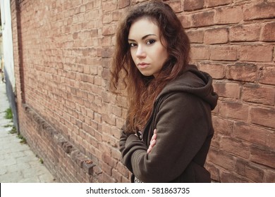 Sad teen girl. Introvert girl with long brown hair near the brick wall. Troubled teen on the street