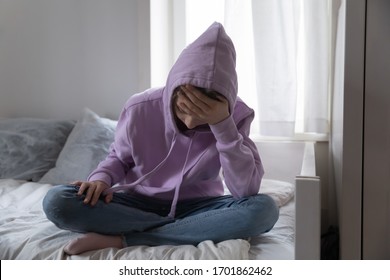 Sad Teen Girl Wears Hood Sitting On Bed Feels Depressed And Lonely. Worried Of Problem At School. Upset Antisocial Adolescent Teenager Suffering From Pain Thinking Of Suicide Crying Alone At Home.