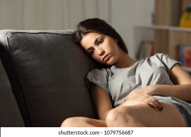 Sad teen looking away sitting on a couch in the living room at home