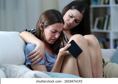 Sad Teen With Phone Being Comforted By Her Sister On A Couch In The Living Room At Home 