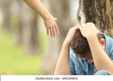 Sad teen sitting on the grass in a park and a woman hand offering help with a green background