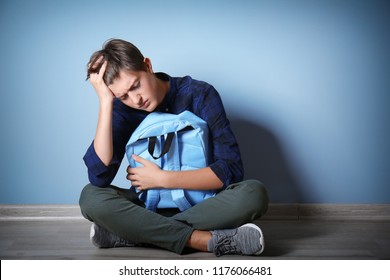 Sad teenage boy sitting on floor indoors. Bullying at school