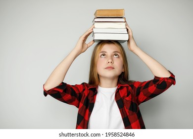 Sad teenage girl holding many books on her head, educational difficulties. A heavy burden of training.