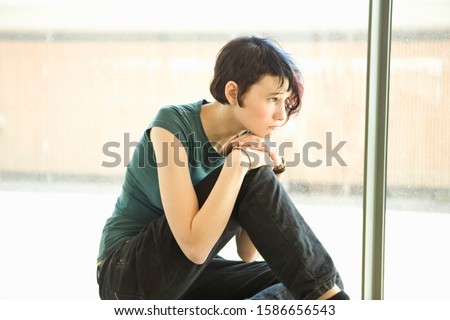 Sad teenage girl sitting alone in front of window