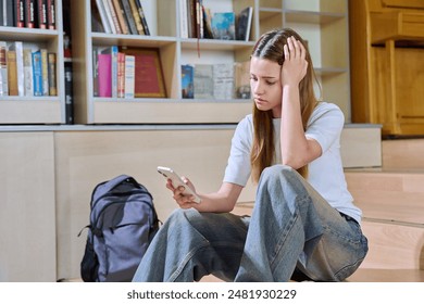 Sad teenage girl student looking at smartphone screen inside high school classroom - Powered by Shutterstock