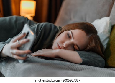 Sad teenage girl suffering from insomnia surfing Internet or chatting using smartphone at night lying on bed. Depression Internet addiction. Young woman depression - Powered by Shutterstock