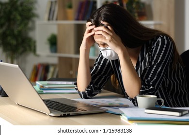 Sad teleworker woman wearing mask with problems due coronavirus sitting on a desk with laptop in the night at home office
