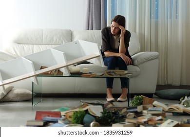 Triste inquilino quejándose luego del robo en su casa sentado en un sofá en la noche con un desordenado salón