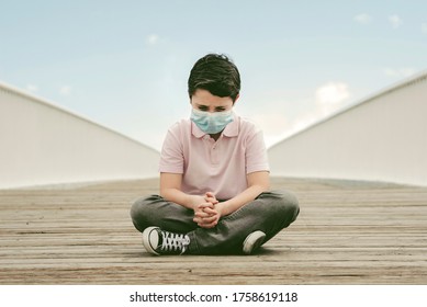 Sad And Thoughtful Kid Wearing Medical Mask Sitting On The Ground